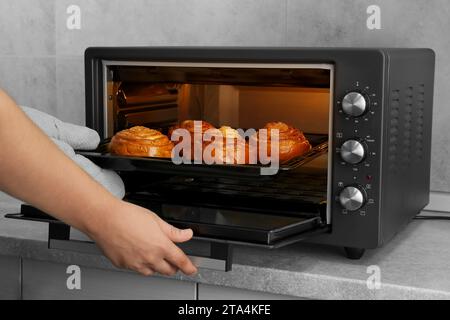 Primo piano: Donna che toglie la teglia da forno con deliziosi panini a spirale dal forno elettrico Foto Stock