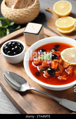 Zuppa di solyanka di carne con salsicce, olive e verdure in ciotola servita su tavola grigia, primo piano Foto Stock