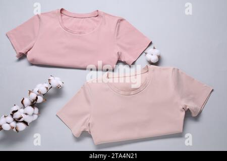 Rametto di cotone con fiori soffici e t-shirt su sfondo grigio chiaro, piatto Foto Stock