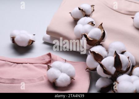 Rametto di cotone con fiori soffici e t-shirt su sfondo grigio chiaro, primo piano Foto Stock