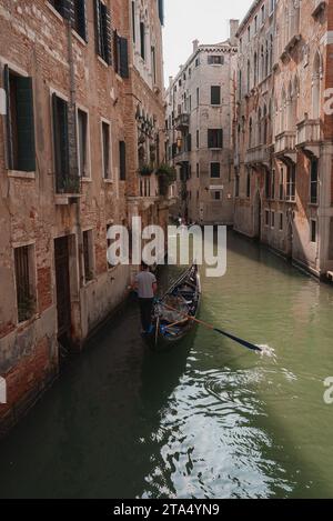 Una gondola vuota che scivola lungo lo stretto canale di Venezia, Italia - scena serena e senza tempo Foto Stock