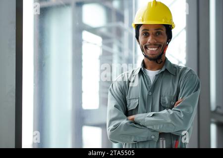 Ritratto di un lavoratore edile sorridente e sicuro in hardhat e tuta grigia Foto Stock