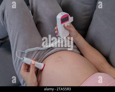 Primo piano della pancia di una donna incinta usando un doppler domestico. Schermo vuoto. Foto Stock