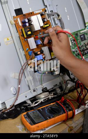 Cairo, Egitto, 3 ottobre 2023: Ingegnere tecnico che utilizza un multimetro digitale, circuito di alimentazione della scheda principale TV LCD, fili, trasformatori, resis Foto Stock