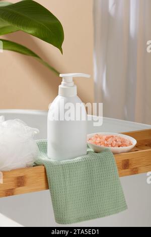 Bottiglia di colore bianco decorata con una spugna da bagno e un piccolo piatto di sale rosa dell'himalaya. Bottiglia cosmetica bianca per crema viso, detergente, corpo Foto Stock