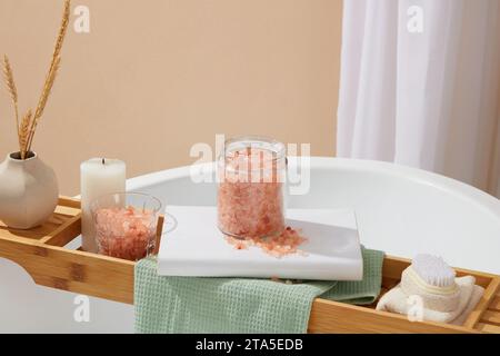 Bagno con vasetto di sale rosa dell'himalaya, fornito con altri accessori sul vassoio della vasca in legno Alcuni sostengono che il sale himalayano sia più nat Foto Stock