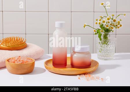 Barattolo e bottiglia senza marchio di colore rosso sfumato decorati con una spazzola, una ciotola di sale rosa dell'himalaya e vaso di fiori. Vista frontale. Concetto di cura della pelle con Foto Stock