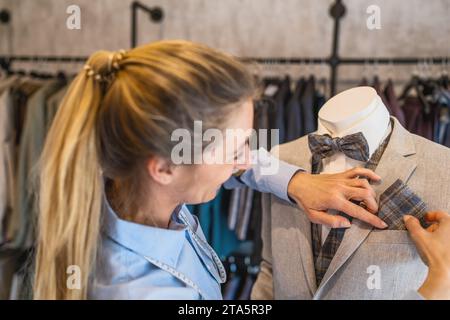 tailor regola una tasca quadrata su un manichino vestito da abito e cravatta in un negozio di matrimoni Foto Stock