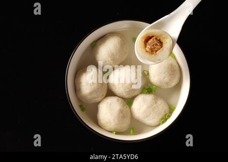 Un mestolo bianco che mescola una pentola di zuppa calda fatta in casa con gnocchi soffici che ribollono Foto Stock