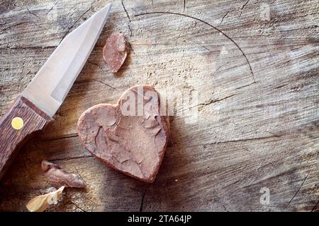 Cuore in legno intagliato e coltello su vecchio sfondo in legno. Romantico concetto d'amore Foto Stock