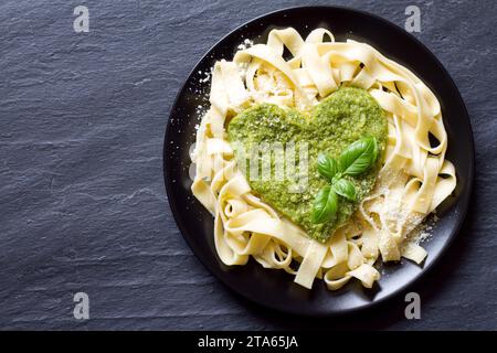 Tagliatelle di pasta con pesto a forma di cuore servite in piatto su fondo scuro, cibo con concetto di amore Foto Stock