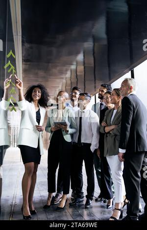 Gruppo multirazziale di uomini d'affari che hanno una riunione in un corridoio di uffici. Giovane dirigente donna che spiega e parla in un incontro informale Foto Stock