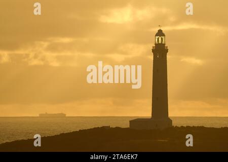 Faro di Cape Leeuwin in luce dorata a con una nave in mare vicino al tramonto vicino alla città di Augusta, nel sud-ovest dell'Australia Occidentale. Foto Stock