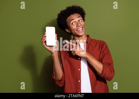 Ritratto di un ragazzo divertente indossa una camicia elegante che dirige l'occhiata al codice qr sullo schermo dello smartphone spazio vuoto isolato su sfondo di colore verde Foto Stock