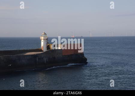 Naviga davanti al faro del molo nord all'ingresso del porto di Aberdeen in Scozia in prima serata, con generatori di vento all'orizzonte Foto Stock