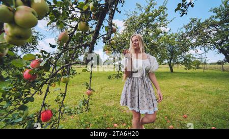 Una ragazza con un vestito bianco che cammina tra un frutteto di mele. Foto Stock