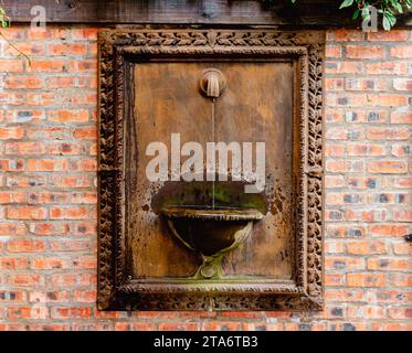 Tipo a fontana. Fontana a muro con beccuccio dell'acqua - struttura in metallo con fontana contro parete in mattoni con acqua che scorre Foto Stock