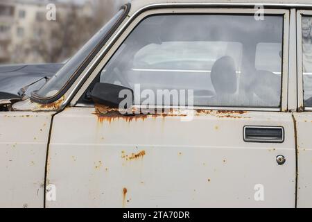 Corrosione della lamiera sulla ruota della vecchia auto bianca. Superficie arrugginita e disordinata. Grana sporca danneggiata dal sale della strada. Sfondo ruggine. Protezione di a Foto Stock