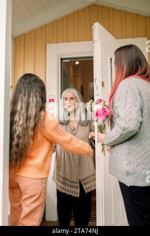 Donna anziana felice che dà il benvenuto alla figlia e alla nipote all'ingresso della casa Foto Stock