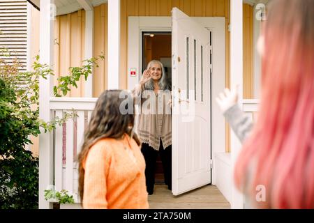 Donna anziana che salta la mano alla nipote dall'ingresso della casa Foto Stock