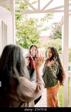 Donna anziana che salta la mano alla figlia e alla nipote dall'ingresso della casa Foto Stock