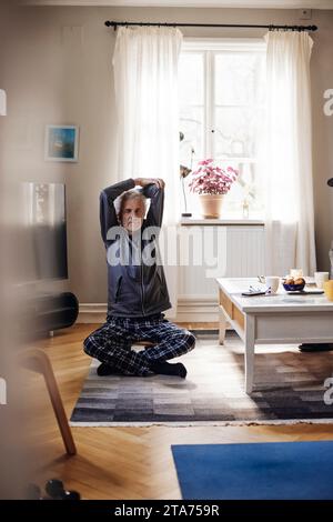 Uomo anziano che allunga le braccia mentre fa yoga in salotto a casa Foto Stock