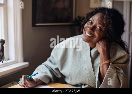 Ritratto di donna matura sorridente in accappatoio che tiene la penna a casa Foto Stock