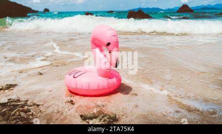 Piccolo anello salvagente in gomma rosa sulla spiaggia. Un anello di nuoto a forma di fenicottero rosa, sulla sabbia di una spiaggia, con l'oceano sullo sfondo. Foto Stock