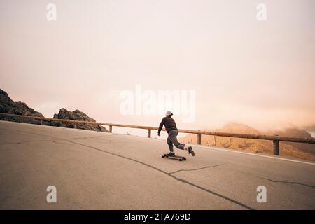 Giovane skateboard su strada vicino a ringhiere contro il cielo Foto Stock