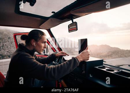 Vista laterale dell'uomo con cuffie intrauricolari wireless che utilizzano un computer portatile mentre si è seduti in un furgone in vacanza Foto Stock