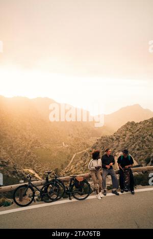 Giovani amici maschi e femmine che parlano seduti a bordo strada al tramonto in vacanza Foto Stock