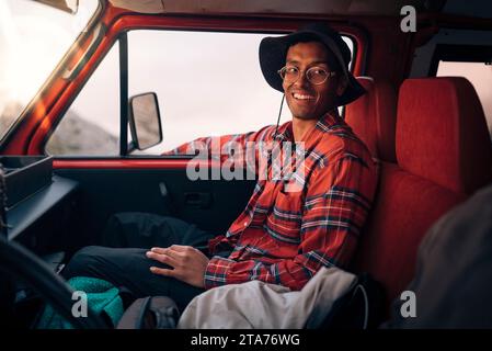 Un giovane sorridente che indossa una camicia a quadri mentre è seduto nel furgone in vacanza Foto Stock