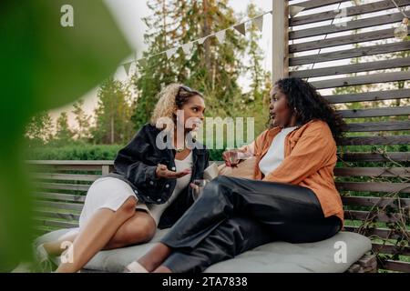 Giovane donna che parla con un'amica mentre si siede seduta nel cortile posteriore Foto Stock
