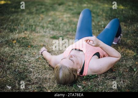 Donna stanca sdraiata sull'erba al parco Foto Stock