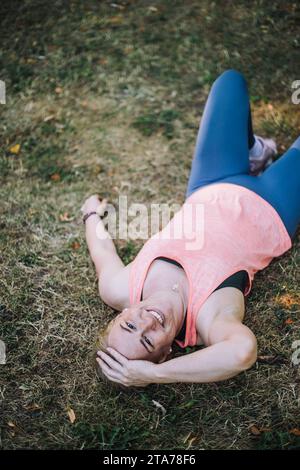 Ritratto di una donna sorridente con la testa in mano sdraiata sull'erba al parco Foto Stock