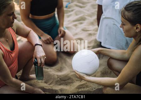 Vista dall'alto della donna che tiene un pallavolo con gli amici inginocchiati sulla sabbia Foto Stock