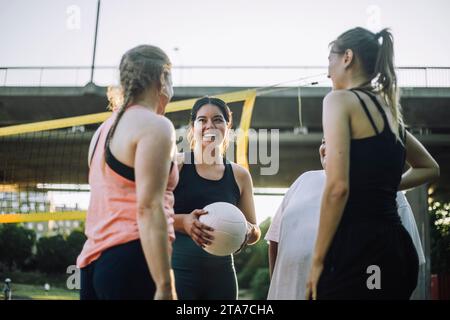 Vista dall'angolo basso di una donna sorridente che tiene una pallavolo con amici femminili Foto Stock