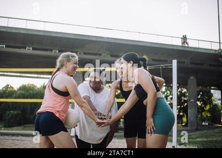 Sorridenti amiche che si impilano le mani mentre giocano a pallavolo Foto Stock