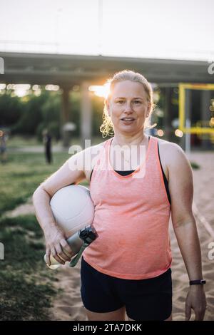 Ritratto di una donna che tiene una bottiglia d'acqua e un pallavolo sotto il braccio Foto Stock