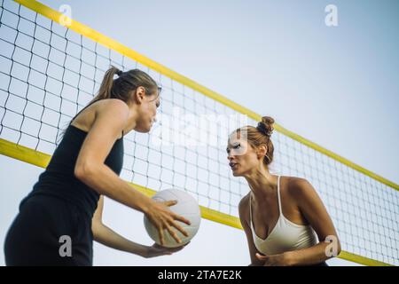 Vista angolare bassa delle amiche che giocano a pallavolo vicino alla rete Foto Stock