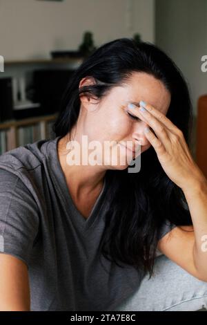 Donna stressata che tocca la fronte mentre è seduta a casa Foto Stock