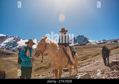 Guida nativa con turista a cavallo con abiti tradizionali durante il tour a piedi della colorata montagna Arcobaleno vicino a Cusco, in Perù Foto Stock