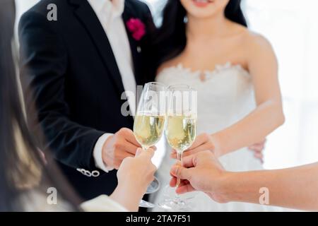 Primo piano di brindisi nuziali con champagne, un allegro allegro al ricevimento di nozze tra amici. Gli sposi e gli sposi asiatici salutano e brindano con gli amici Foto Stock