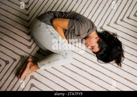 Direttamente sopra la donna solitaria sdraiata in posizione fetale sul tappeto a casa Foto Stock