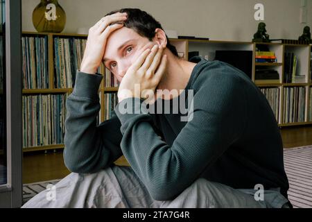 Un giovane depresso che guarda lontano mentre è seduto a casa Foto Stock