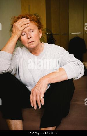 Donna anziana preoccupata seduta con la testa in mano a casa Foto Stock