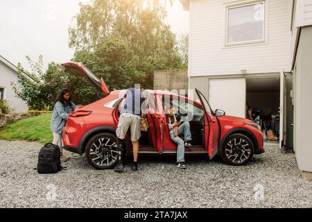 La famiglia sta caricando le cose in un'auto elettrica vicino a casa Foto Stock