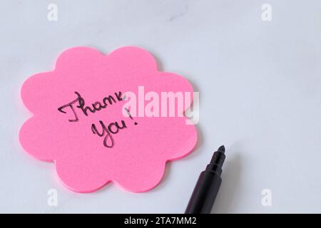 Grazie testo scritto a mano su una nota adesiva rosa a forma di fiore con marcatore nero su bianco.Copia spazio. Concetto di gratitudine, apprezzamento e rispetto. Foto Stock
