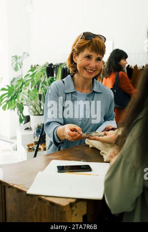 Una cliente sorridente che effettua pagamenti online tramite carta di credito mentre fa acquisti in un negozio di abbigliamento Foto Stock