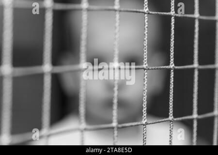 Faccia sfocata, giovane ragazzo dietro la corda della rete. Concetto di sicurezza. Bianco e nero. Monocromatico. Foto Stock